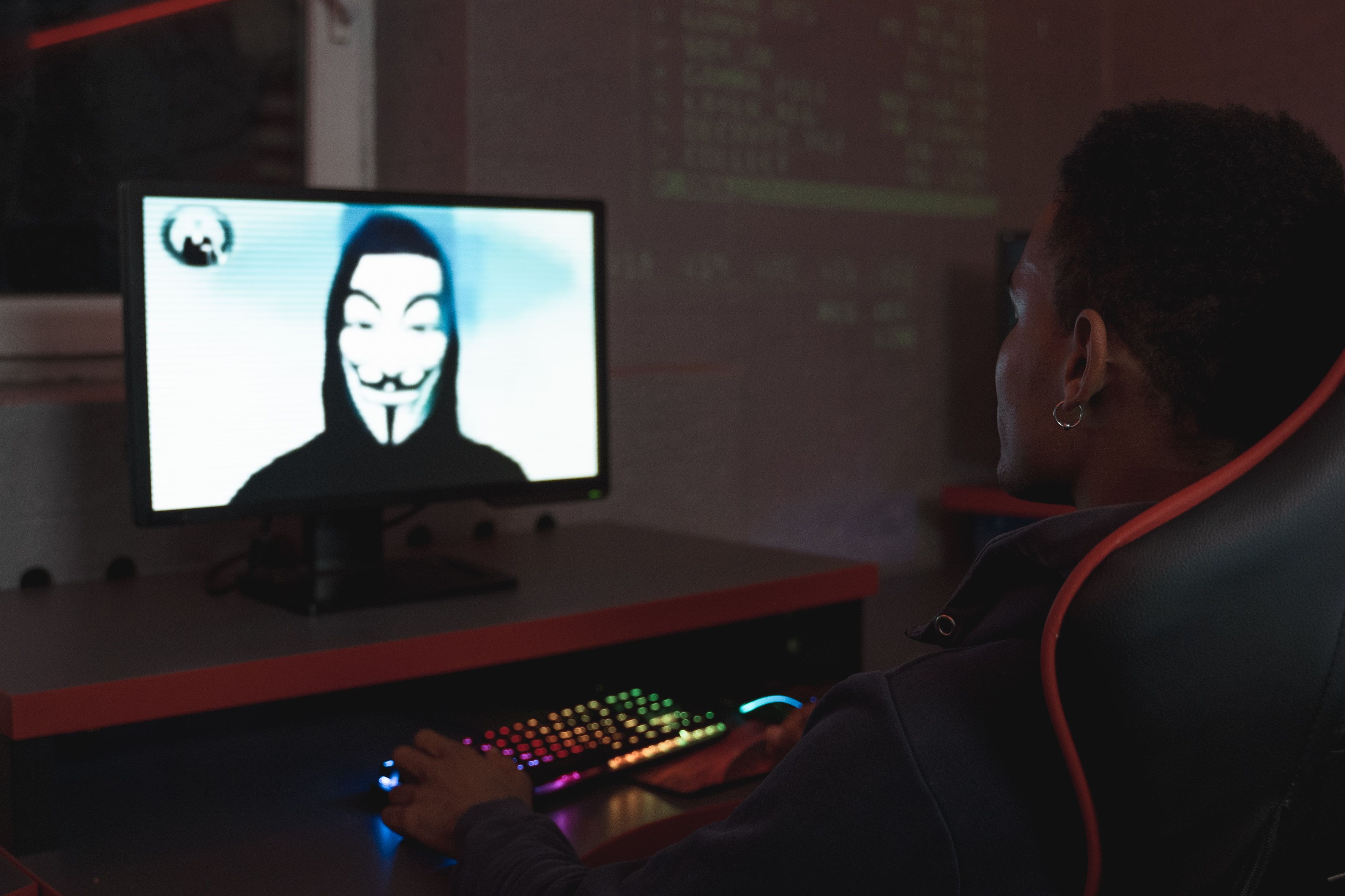 Person viewing a masked hacker on a computer screen, symbolizing cybersecurity threats and personal data breaches
