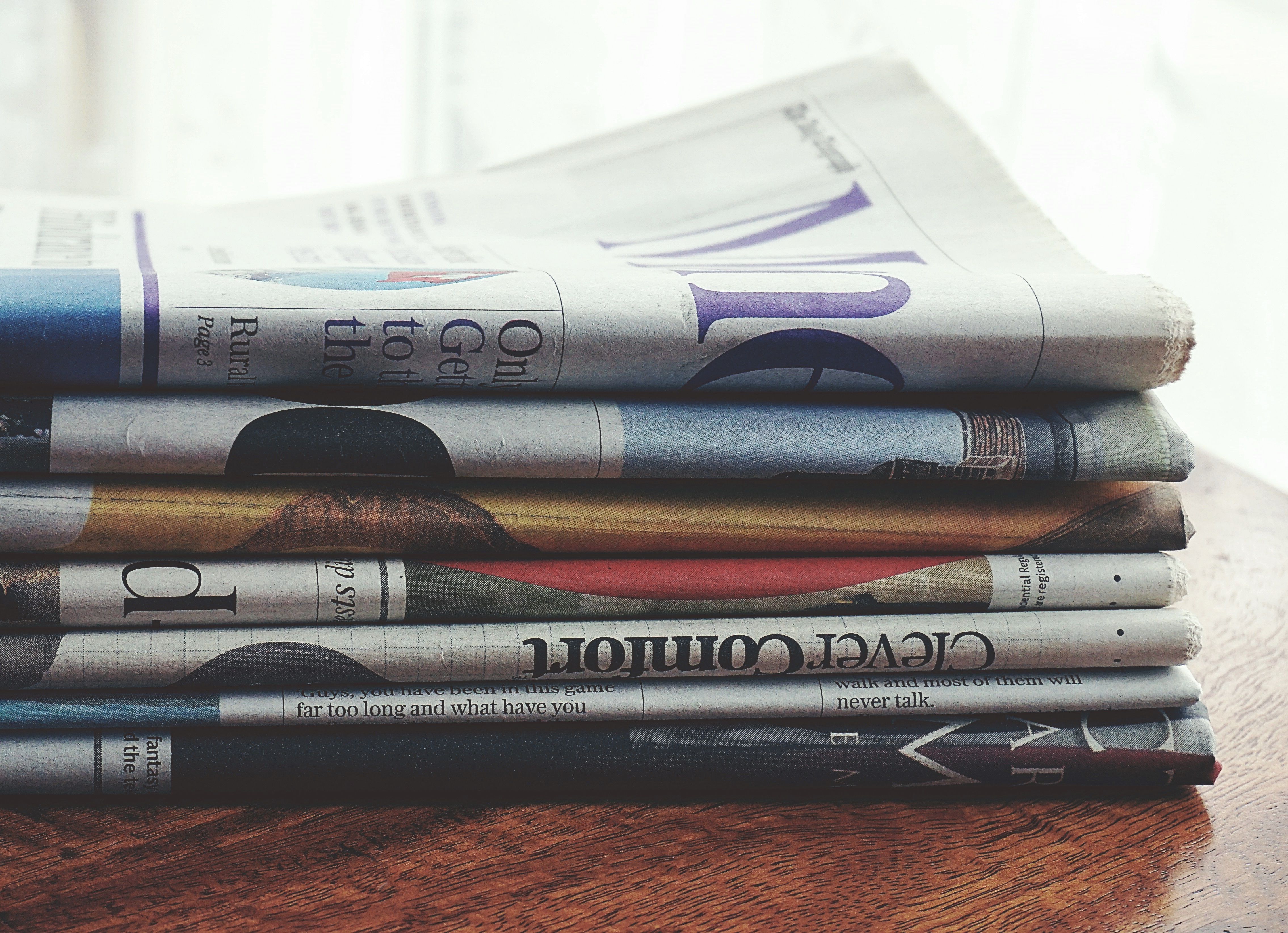 Stack of folded newspapers on a wooden table representing scandal headlines and news cycles