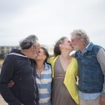 A senior couple and a younger couple sharing affectionate moments on a beach, representing relationships across age groups.