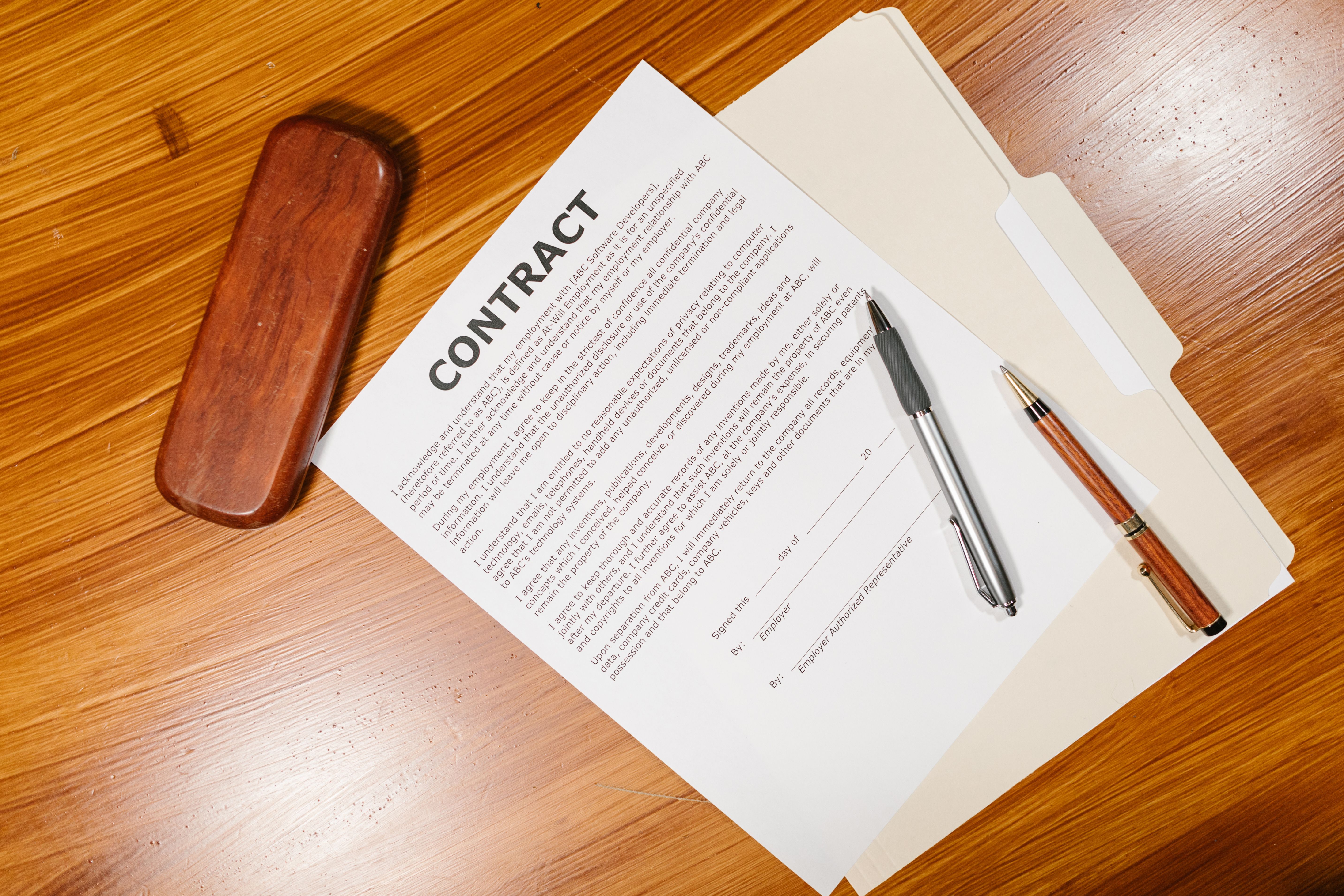 Contract documents, pens, and a case on a wooden table, representing legal paperwork and discovery costs.